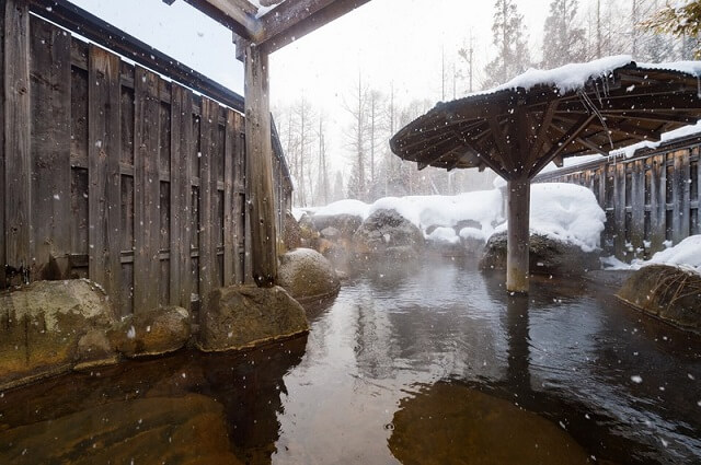 温泉の露天風呂に雪が降る様子